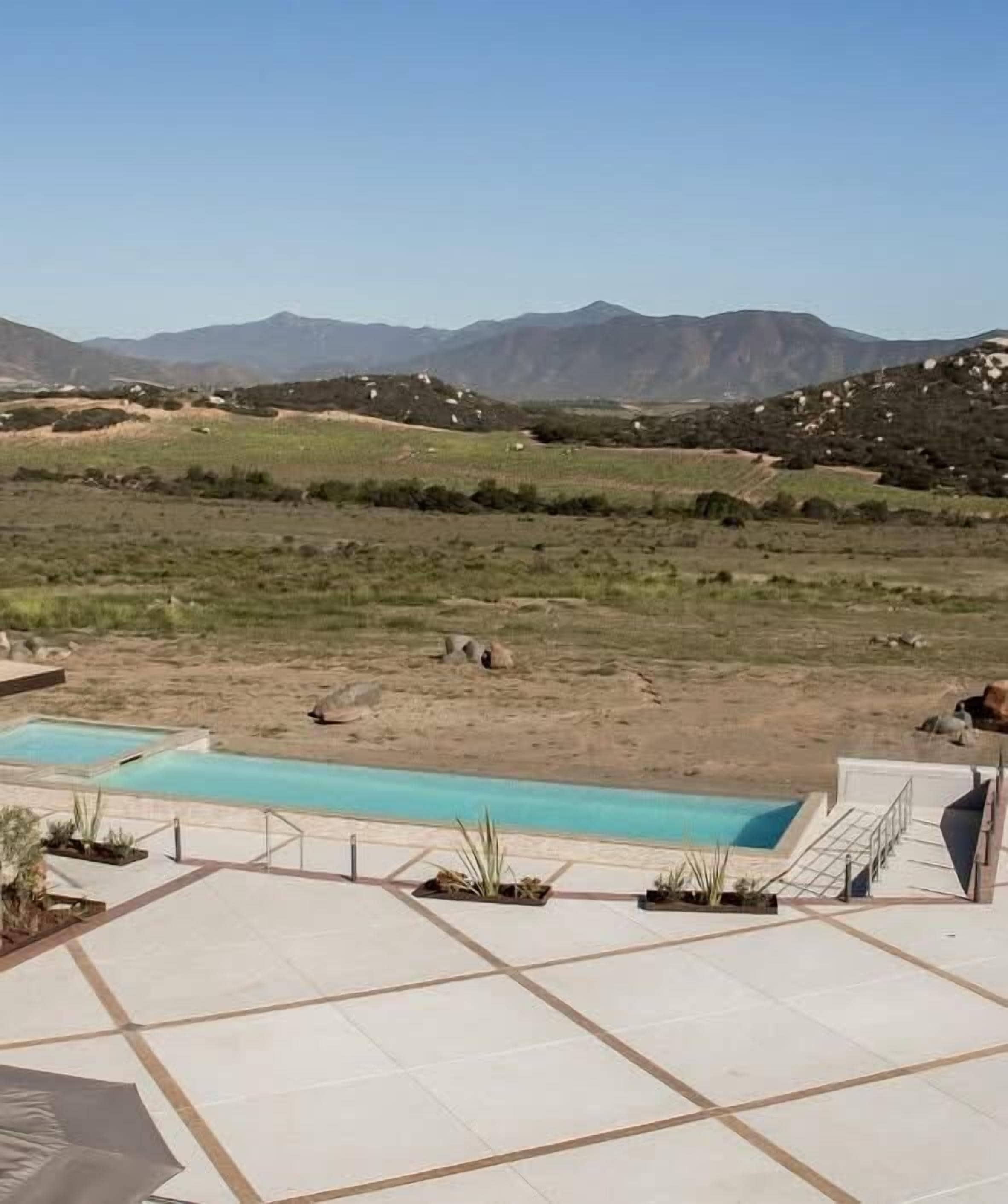 A pool area with a view of mountains, a clear sky, and a landscaped garden.