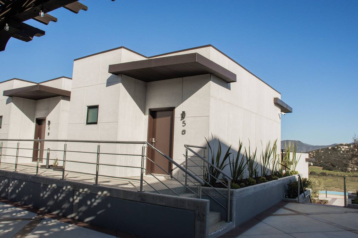 A modern building with a flat roof, a staircase leading to an entrance, and a view of the landscape in the background.