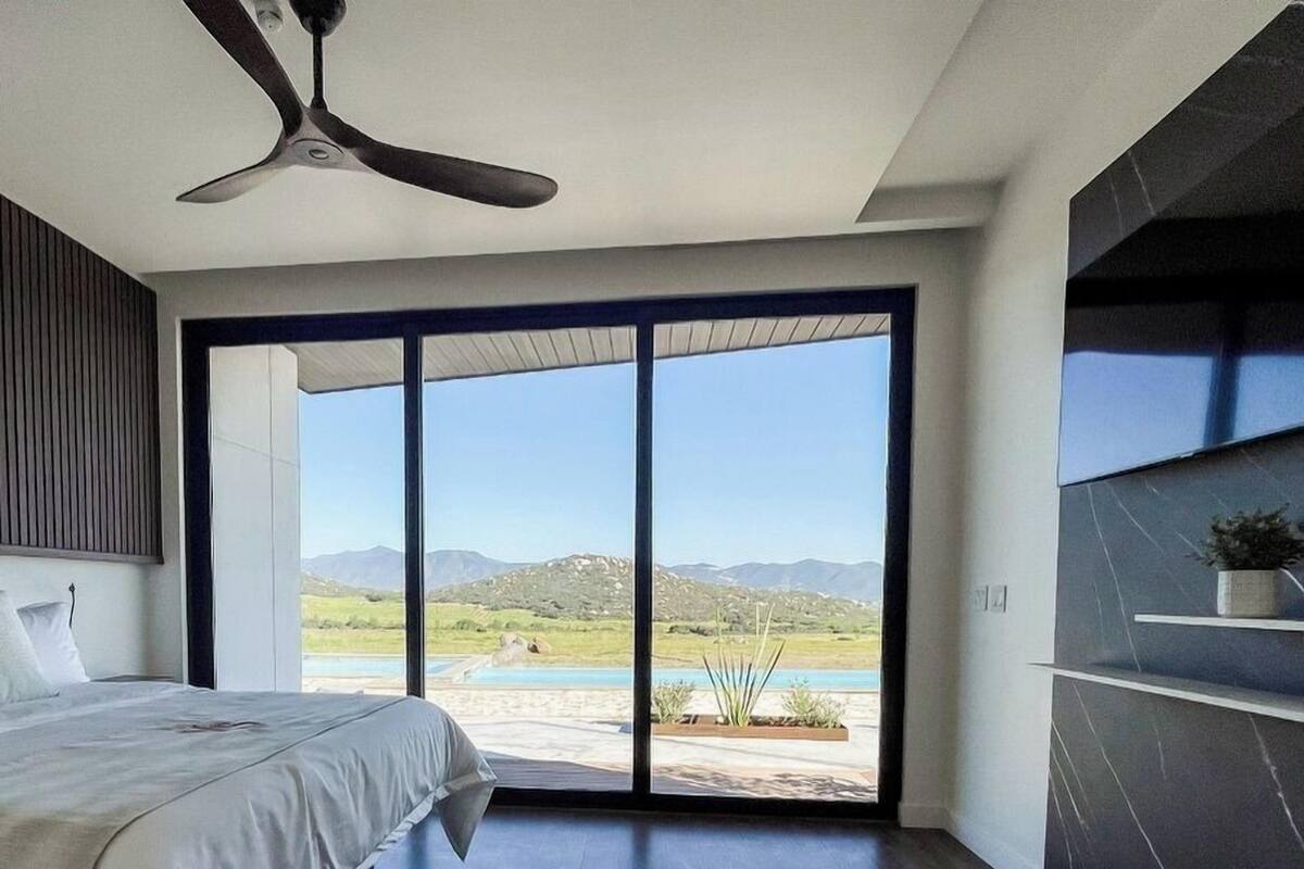 A modern bedroom with a bed, a ceiling fan, and a large sliding glass door leading to a pool area.