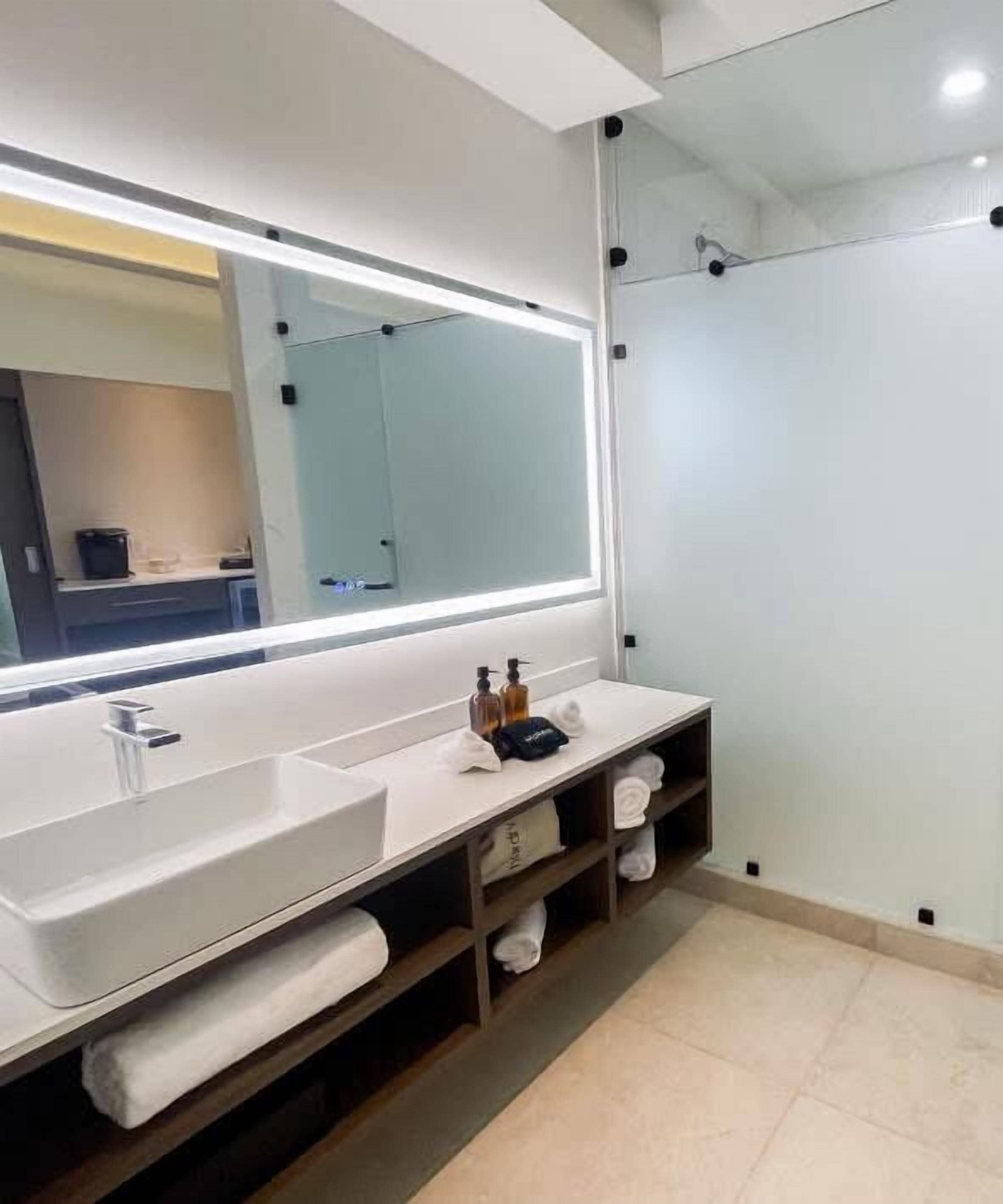 A modern bathroom with a large mirror, a sink, and a shower area.