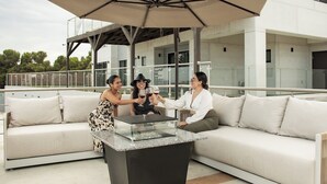 A modern outdoor seating area with a glass-top table, a large umbrella, and a white sofa. - VILLA SIMUL HOTEL BOUTIQUE VALLE DE GPE (Valle de Guadalupe)