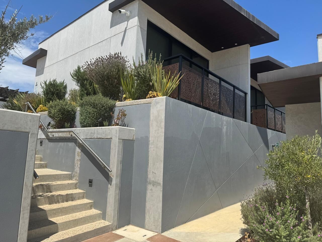 A modern building with a concrete facade, a staircase leading to an upper level, and a variety of plants.