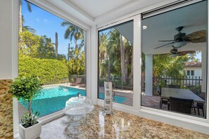 A poolside area with a glass enclosure, a table with chairs, and a ceiling fan. - DREAM BEACH HOUSE With HEATED POOL (Hollywood)