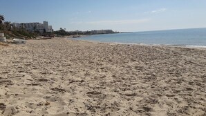 A wide sandy beach with footprints, a calm sea, and buildings in the background. - Independent villa floor, next to the sea! ideal for families (Hammamet)