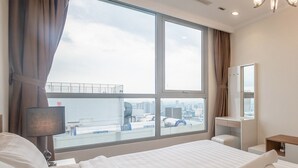 Habitación de hotel con una cama grande, un escritorio, una silla, una lámpara, un espejo y vistas a la ciudad por la ventana.