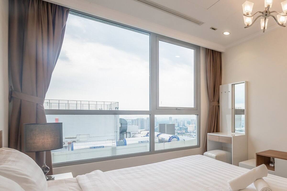 Ein Hotelzimmer mit einem großen Bett, einem Schreibtisch, einem Stuhl, einer Lampe, einem Spiegel und Blick auf die Stadt.