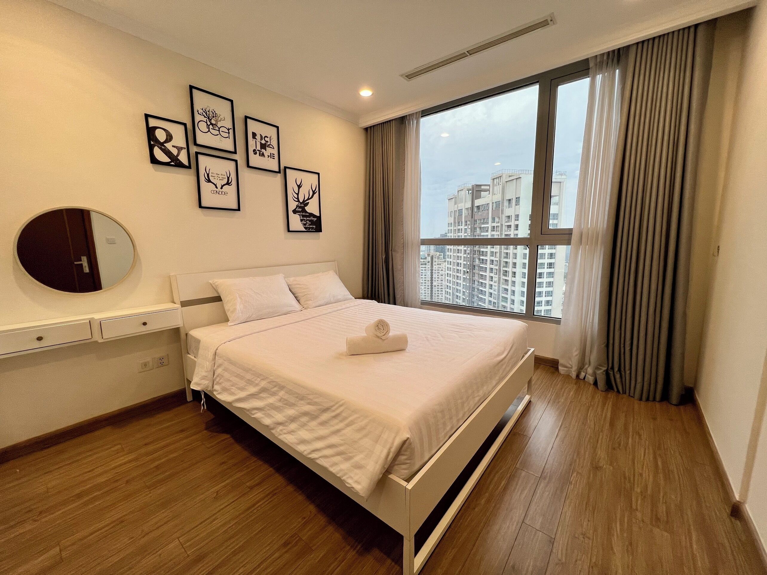Ein modernes Hotelzimmer mit einem großen Bett, einem runden Spiegel und gerahmten Kunstwerken an der Wand.