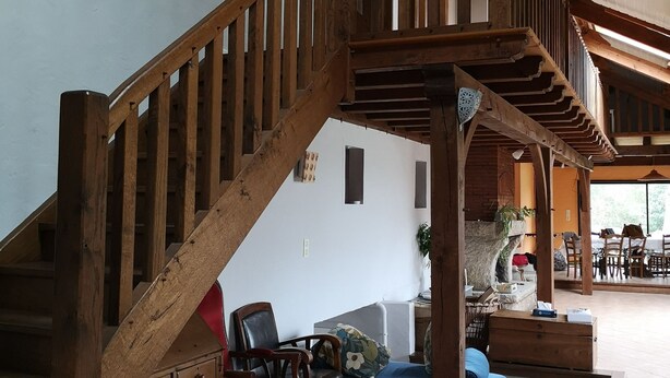A spacious living area with a wooden staircase leading to an upper level, a seating area with a sofa and chairs, and a dining area with tables and chairs.