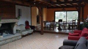 A spacious living area with a stone fireplace, wooden ceiling beams, and a view of the outdoors.