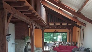 A spacious living area with a high ceiling, wooden beams, a stone fireplace, and a red sofa.