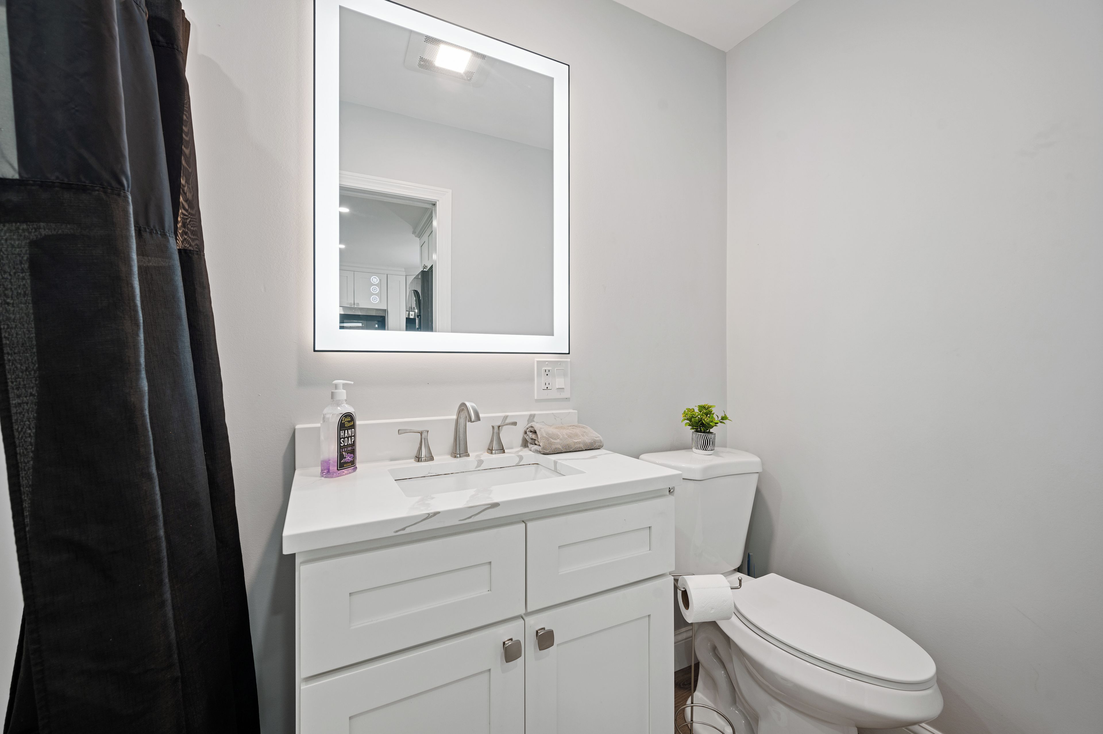 A bathroom with a white sink, a mirror, a toilet, and a shower curtain.