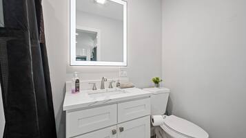 A bathroom with a white sink, a mirror, a toilet, and a shower curtain.