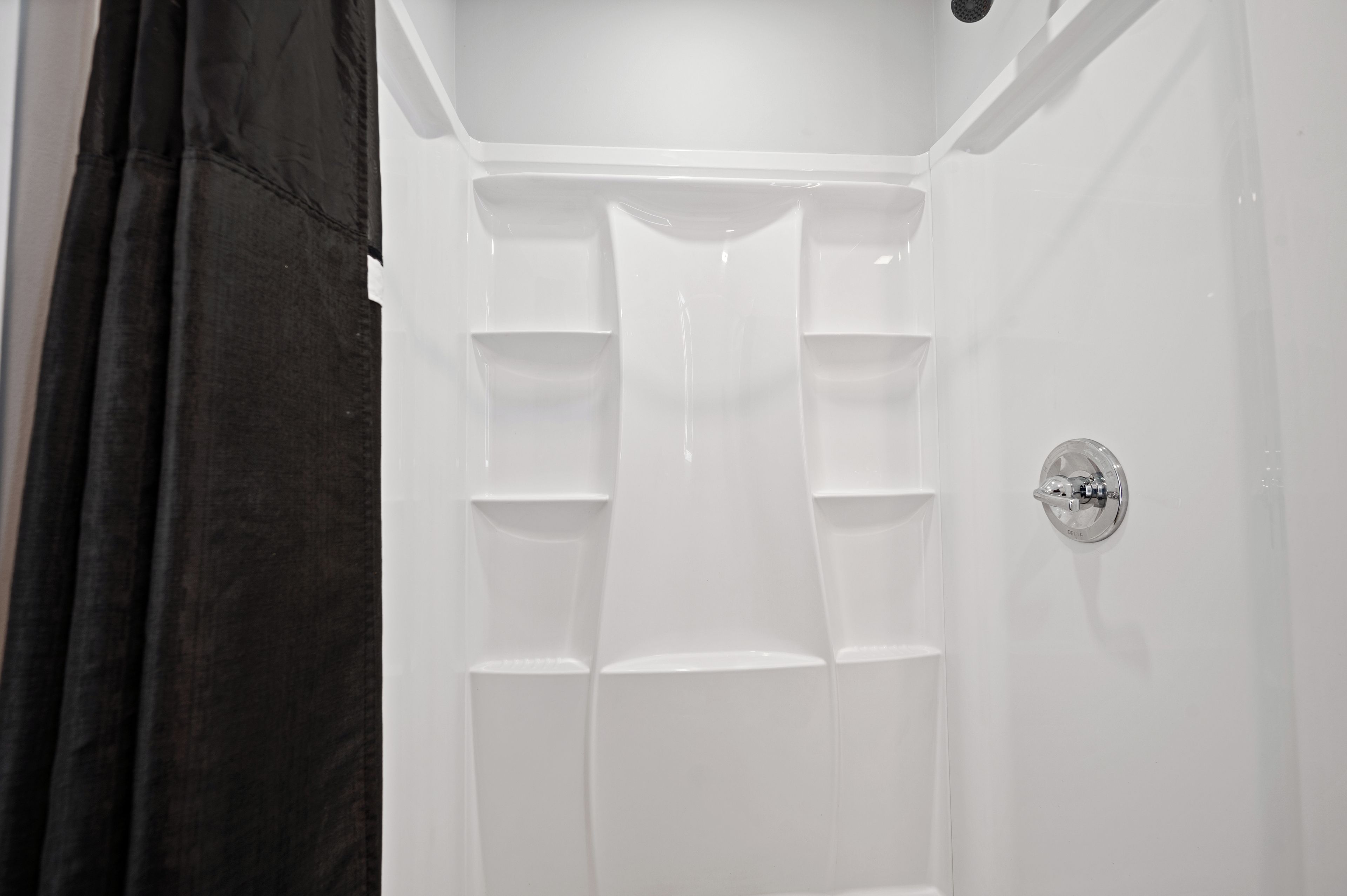 Ducha blanca con grifo Delta y varios estantes para almacenamiento.