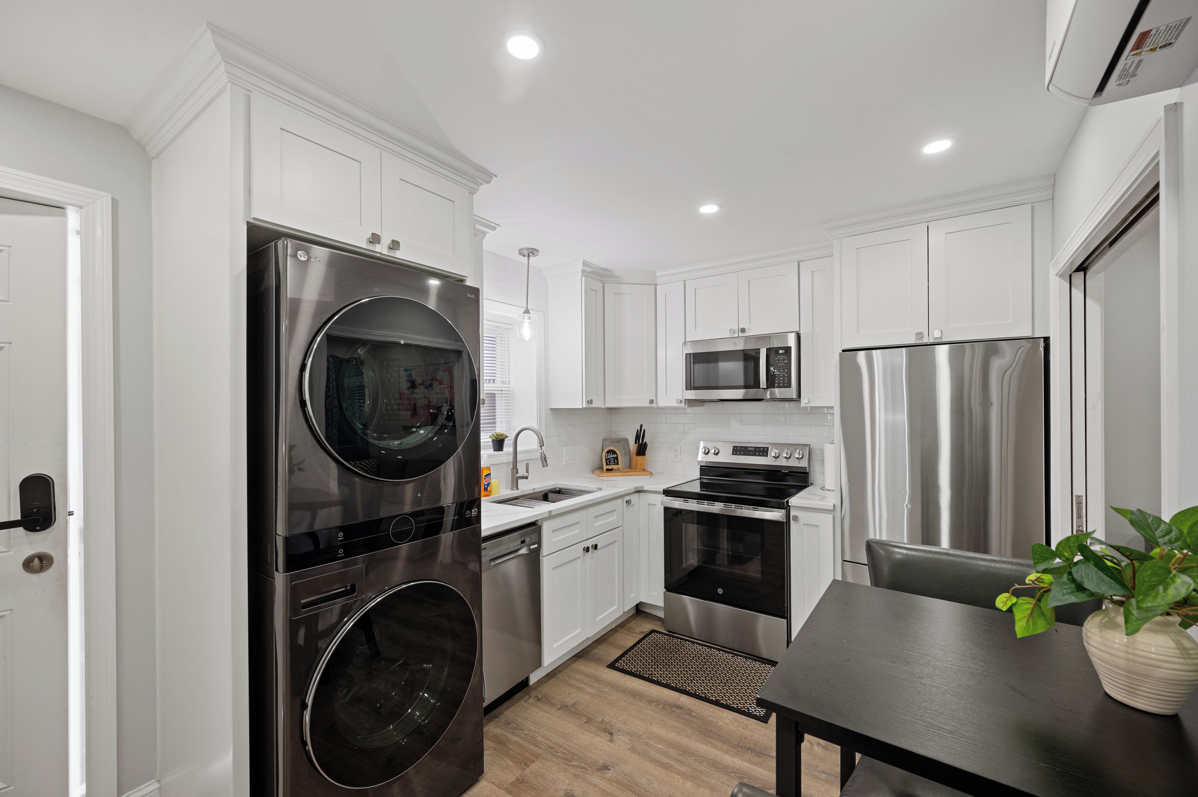 Cocina compacta con armarios blancos, electrodomésticos de acero inoxidable y un pequeño comedor.