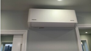 A white air conditioning unit mounted on a wall with a recessed ceiling light above it.