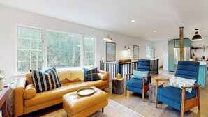 Un salon spacieux avec un canapé en cuir, un fauteuil bleu et une table basse en bois. De grandes fenêtres offrent une vue sur l’extérieur.