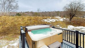 Un bain à remous sur une terrasse, avec vue sur un paysage enneigé et des arbres.