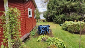 A red wooden house with a small deck and a grill, surrounded by a grassy yard and dense trees. - 5 Person Holiday Home in Karlskoga (Karlskoga)
