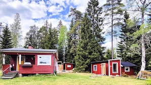A red cabin with a small porch and a window, surrounded by a grassy yard and tall trees. - 5 Person Holiday Home in Karlskoga (Karlskoga)