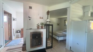 A compact living space with a fireplace, a bed, a refrigerator, and a small table with a lamp. - 5 Person Holiday Home in Karlskoga (Karlskoga)