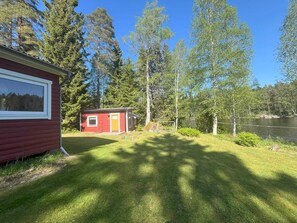 A small red cabin with a window and a door, surrounded by a grassy area and trees, near a body of water. - 5 Person Holiday Home in Karlskoga (Karlskoga)