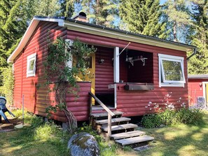 A red log cabin with a front door, a small porch, and a staircase leading to the entrance.