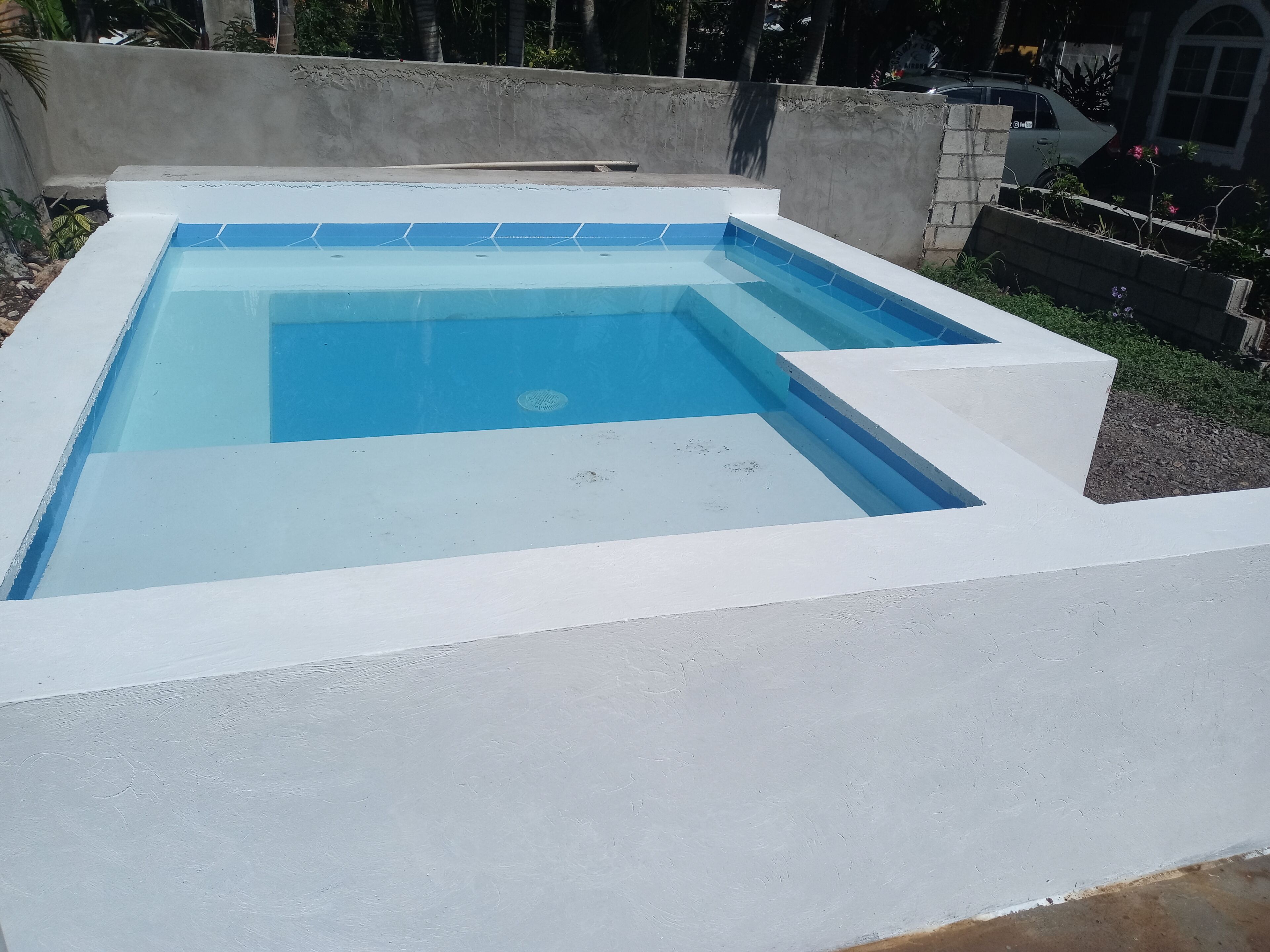 Une piscine rectangulaire avec un bordure blanche et des carreaux bleus au fond.