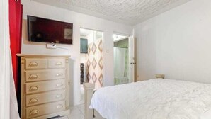 A bedroom with a bed, a dresser, a TV, and a door leading to another room.
