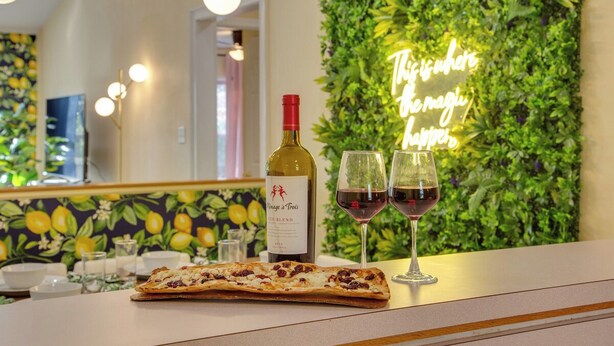 Une scène de restaurant avec une table dressée pour deux personnes, comprenant une bouteille de vin et deux verres, une part de pizza et un panneau lumineux en arrière-plan.