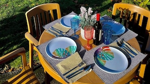 Una mesa de comedor al aire libre con sillas, platos, cubiertos y una botella de vino.