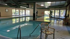 Una piscina interior con paredes de vidrio transparente, suelo de baldosas y una silla cerca del borde.