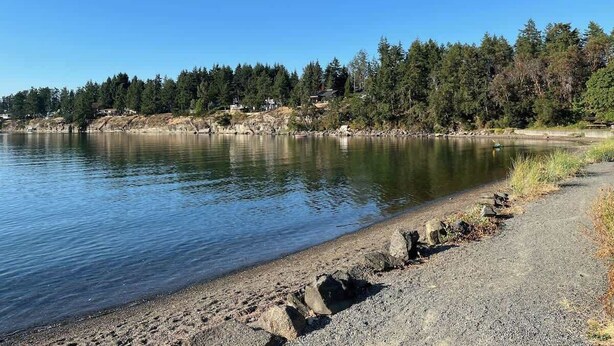 A lakeside view with a gravel path, trees, and a clear sky. - Coastal Elements - 1BDRM - Full Kitchen (Nanoose Bay)