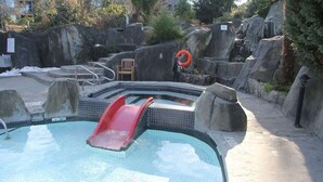 A swimming pool with a red slide, surrounded by rocks and a lifebuoy. - Coastal Elements - 1BDRM - Full Kitchen (Nanoose Bay)
