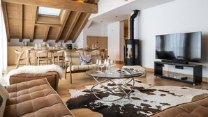 A spacious living area with a high ceiling, a fireplace, a TV, and a dining area with wooden furniture. - Wifi, 150m from ski slopes, 3rd floor, view mountain, sauna, hammam, terrace, balcony (Méribel - Les Allues)
