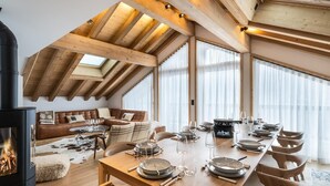 A spacious dining area with a long wooden table set for a meal, a cozy seating area with a leather sofa, and a fireplace. - Wifi, 150m from ski slopes, 3rd floor, view mountain, sauna, hammam, terrace, balcony (Méribel - Les Allues)