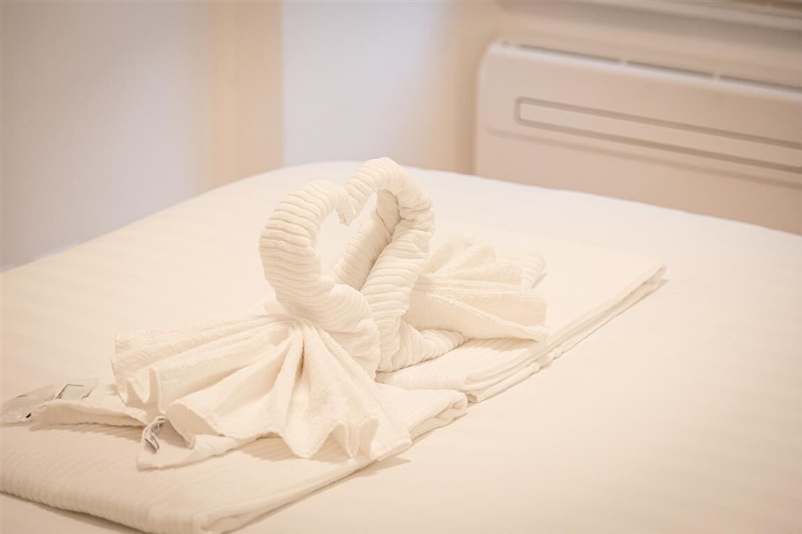 A neatly made bed with a towel arranged in a swan shape.