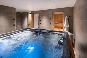 Moderni spa-huone, jossa on suuri poreallas, puiset ovet ja pyyheteline.