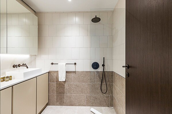 A modern bathroom with a white sink, beige tiles, a shower, and a wooden door.