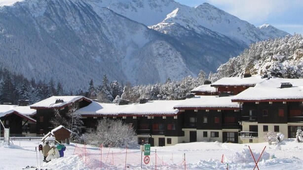 A snow-covered mountain resort with chalet-style buildings, a ski lift, and a clear view of the surrounding mountains.