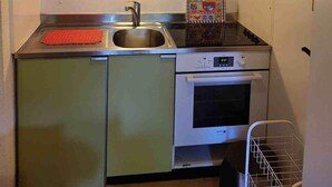 A compact kitchen with green cabinets, a microwave, a stove, and a hanging light fixture.