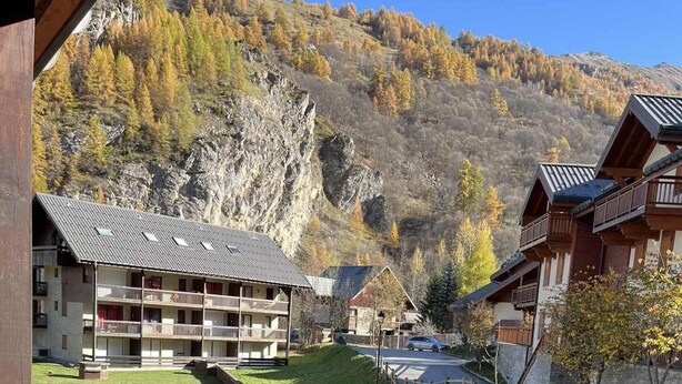 Un chalet de montagne doté de plusieurs balcons, d’un espace de stationnement et offrant une vue sur les collines environnantes.