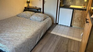 Une chambre comprenant un lit, une table de chevet, une lampe et une petite kitchenette équipée d’un évier et de placards.