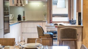 Une cuisine moderne avec un coin repas, comprenant une table à plateau en verre, des chaises et un luminaire suspendu.