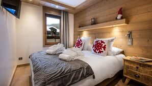 Une chambre à coucher avec un lit, une table de chevet, un téléviseur, une fenêtre avec des rideaux et un mur en bois.