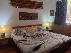 Een slaapkamer met een bed, twee nachtkastjes, een kunstwerk aan de muur en een raam met gordijnen.
