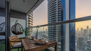 A balcony with a wooden table, chairs, and a hanging chair. It overlooks a cityscape with tall buildings.