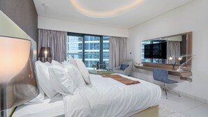 A modern hotel room with a large bed, a desk, a TV, and a view of the city.