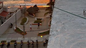 A coastal view with a sunset over the ocean, a paved area with parked motorcycles, and a few people walking.