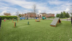 Un'area giochi con diverse attrezzature, un prato verde e un edificio in mattoni sullo sfondo.