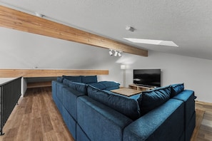 A modern living room with a sectional sofa, a flat-screen TV, and a wooden ceiling beam. - Morning Star Lookout-Spa/Walk to Beach/Ocean Views (Gold Beach)